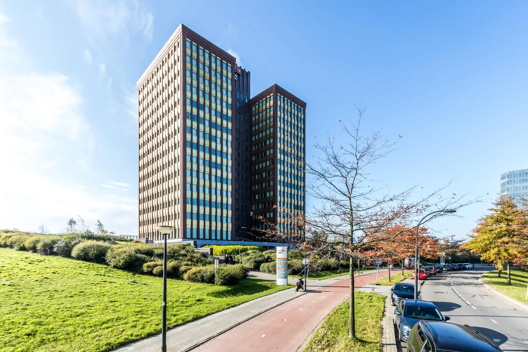 Twee moderne kantoortorens aan de Fascinatio Boulevard met een fietspad, bomen en geparkeerde auto's op de voorgrond.